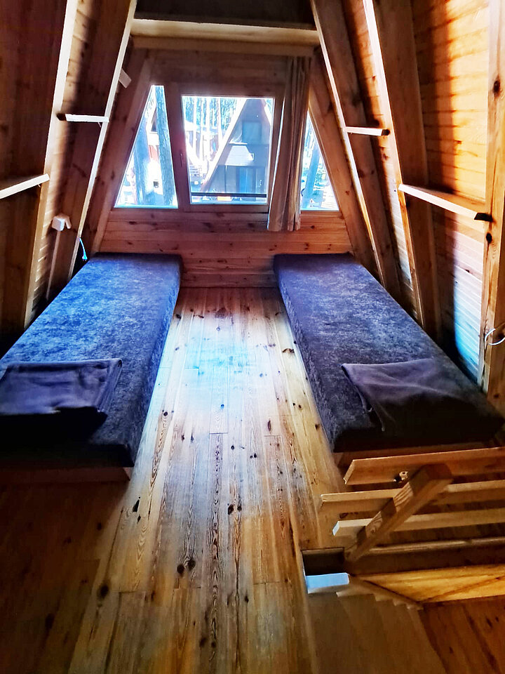 Wnętrze poddasza drewnianego domku turystycznego z mocno spadzistym dachem. Widać dwa jednoosobowe łóżka.